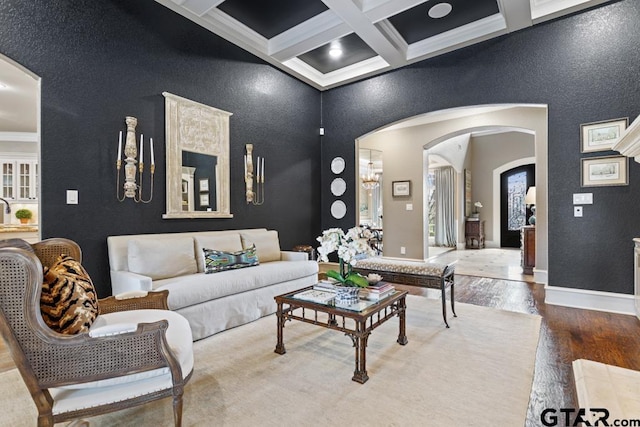 living area with arched walkways, coffered ceiling, wood finished floors, baseboards, and beam ceiling