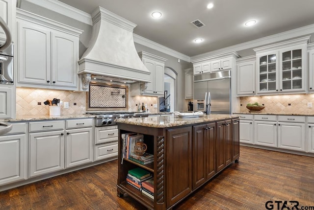 kitchen with a center island, crown molding, custom exhaust hood, visible vents, and appliances with stainless steel finishes