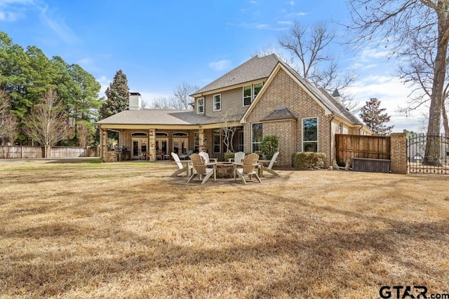 rear view of house with a patio, a fire pit, brick siding, fence, and a yard