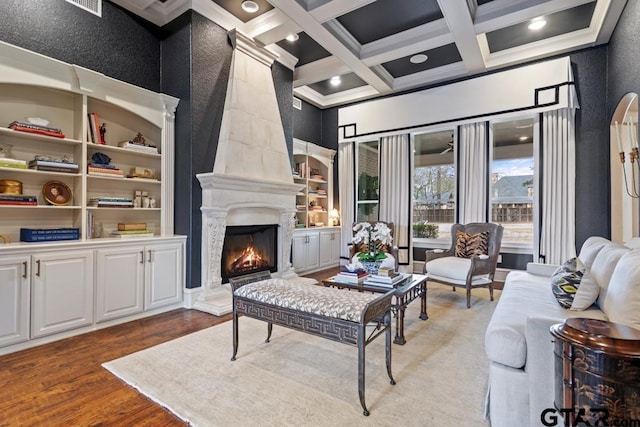 living room featuring a large fireplace, coffered ceiling, wood finished floors, built in shelves, and beam ceiling