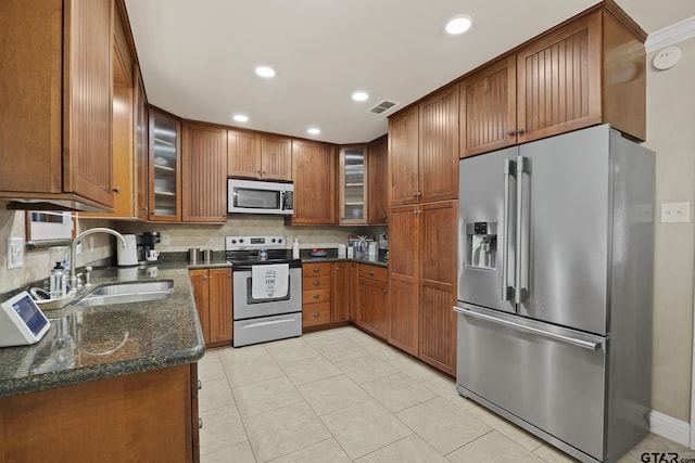 5298 Leaning Oaks Dr, Flint, TX 75762 - kitchen with appliances with stainless steel finishes, a sink, brown cabinetry, dark stone counters, and glass insert cabinets