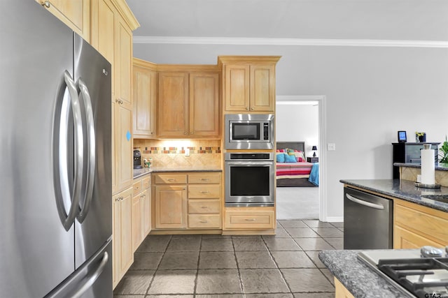 kitchen featuring dark stone countertops, appliances with stainless steel finishes, backsplash, light brown cabinetry, and ornamental molding