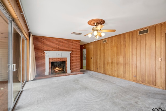 unfurnished living room featuring a fireplace, ceiling fan, wooden walls, and light carpet