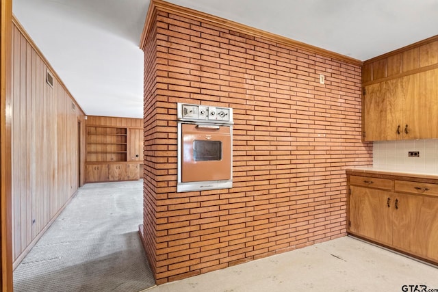 kitchen featuring wood walls, oven, brick wall, and built in features