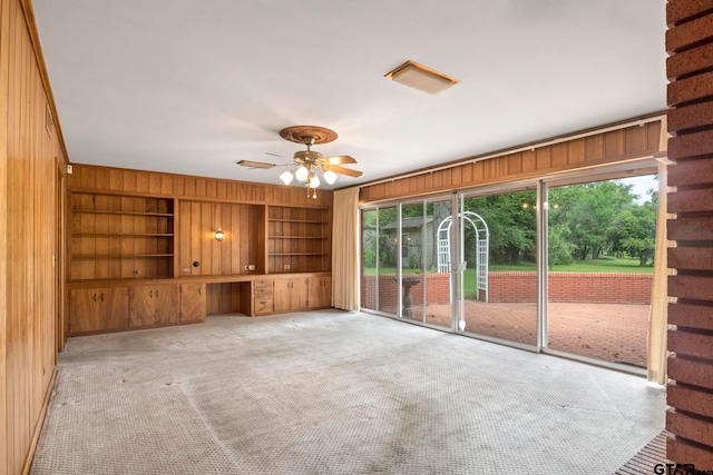 unfurnished living room featuring light colored carpet, wood walls, ceiling fan, and built in features