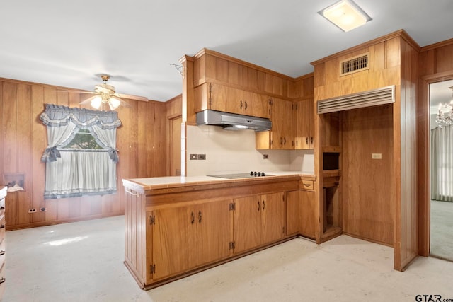 kitchen featuring wood walls, extractor fan, kitchen peninsula, ceiling fan with notable chandelier, and black electric stovetop