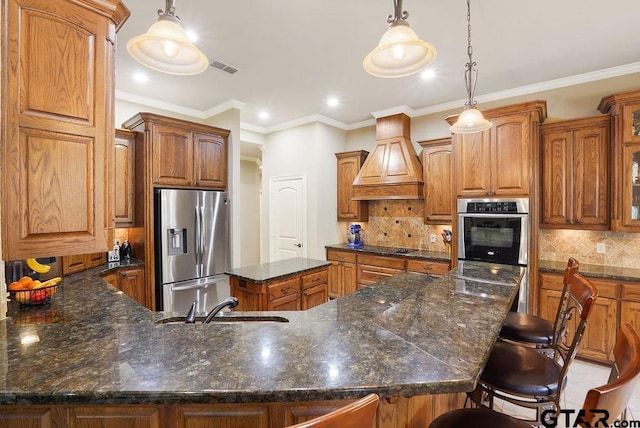 302 Coventry St, Bullard, TX 75757 - kitchen featuring stainless steel appliances, brown cabinets, custom exhaust hood, decorative backsplash, and a kitchen breakfast bar