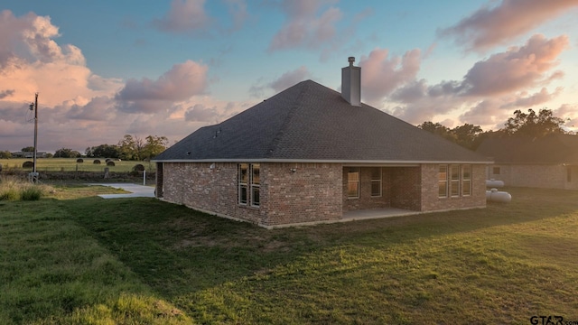 2062 County Road 1612, Alba, TX 75410 - back of property at dusk featuring a patio area, a chimney, a yard, roof with shingles, and brick siding