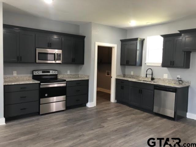 kitchen featuring stainless steel appliances, sink, light stone counters, and dark hardwood / wood-style flooring