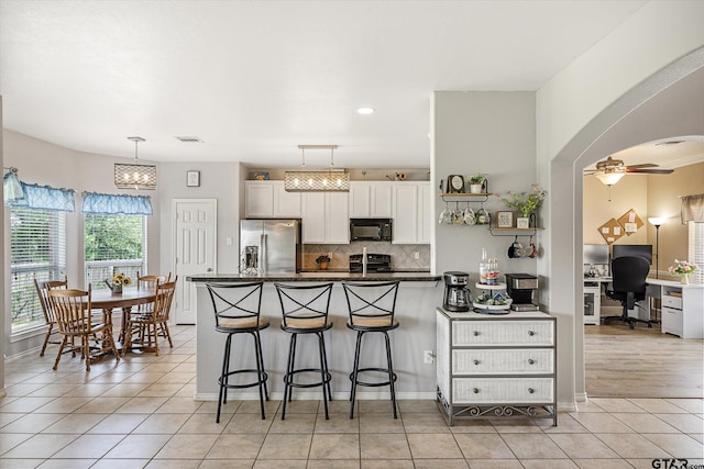 kitchen featuring a kitchen bar, ceiling fan, black appliances, white cabinets, and hanging light fixtures