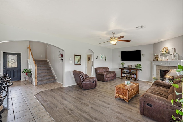 living room featuring ceiling fan, a tile fireplace, and light hardwood / wood-style flooring