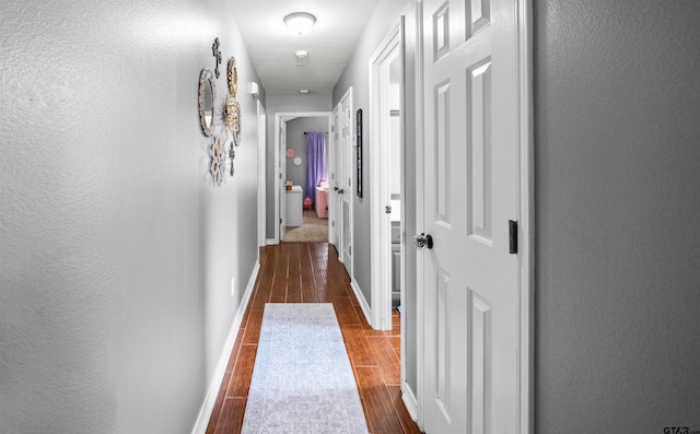 hall featuring a textured wall, baseboards, and wood finish floors