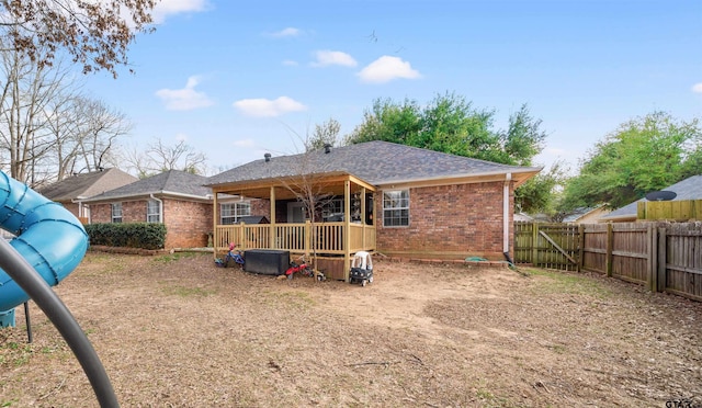 rear view of house with brick siding, roof with shingles, and fence