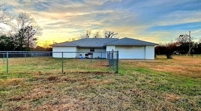 back house at dusk with a garage and a lawn