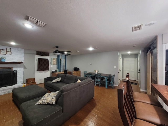 living room with a brick fireplace, dark wood-type flooring, and ceiling fan