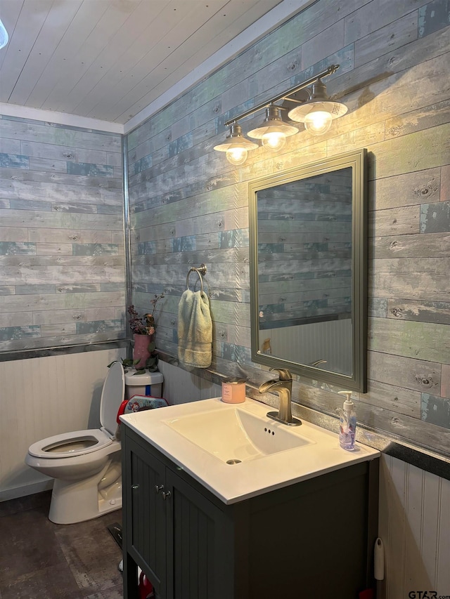 bathroom featuring wood walls, wooden ceiling, vanity, and toilet