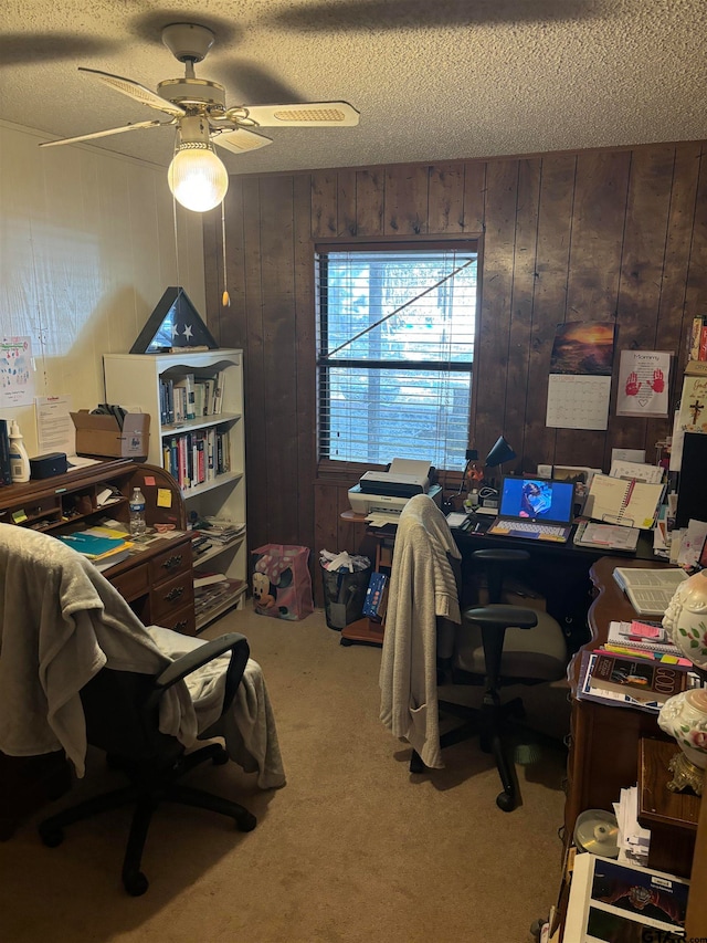 carpeted office space featuring a textured ceiling, wood walls, and ceiling fan