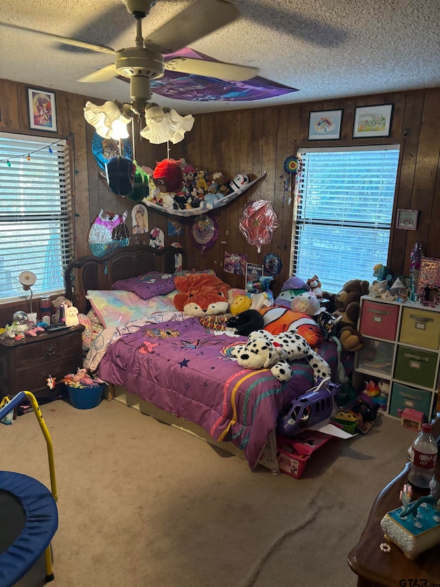 carpeted bedroom with multiple windows, ceiling fan, wooden walls, and a textured ceiling