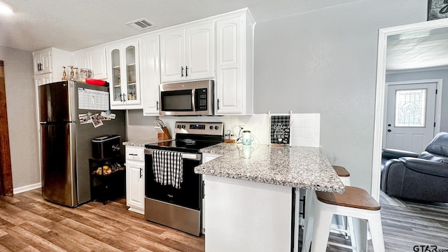 kitchen with stainless steel appliances, light hardwood / wood-style floors, white cabinetry, a kitchen breakfast bar, and light stone countertops