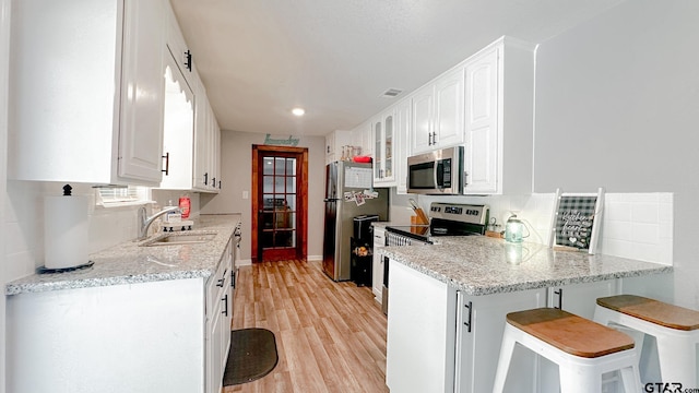 kitchen with white cabinetry, appliances with stainless steel finishes, sink, and light stone countertops