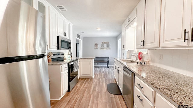 kitchen with light stone countertops, white cabinetry, light wood-type flooring, and appliances with stainless steel finishes