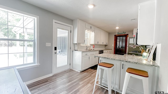 kitchen with white cabinetry, a wealth of natural light, a kitchen bar, and light hardwood / wood-style flooring