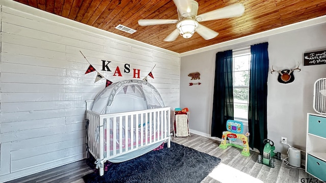 bedroom with wood ceiling, wooden walls, hardwood / wood-style flooring, a crib, and ceiling fan