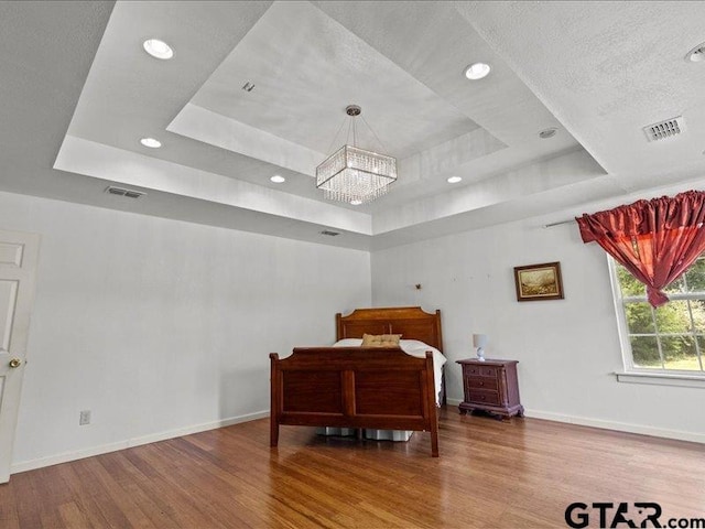 bedroom featuring hardwood / wood-style floors, a chandelier, a textured ceiling, and a raised ceiling