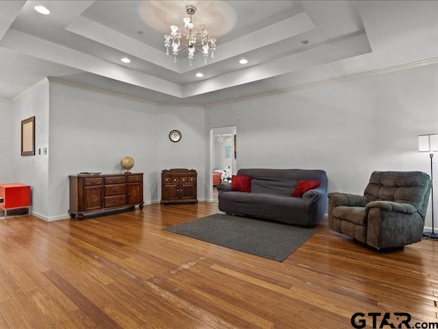 living room featuring wood-type flooring, ornamental molding, a chandelier, and a tray ceiling