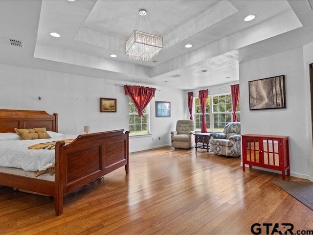 bedroom featuring hardwood / wood-style floors, a notable chandelier, and a tray ceiling