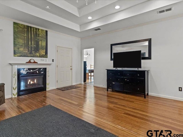 living room with a notable chandelier, wood-type flooring, crown molding, and a tray ceiling