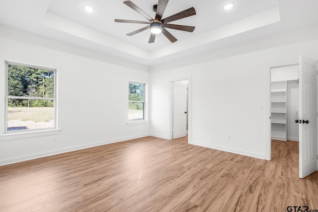 unfurnished bedroom with light wood-style flooring, baseboards, and a tray ceiling