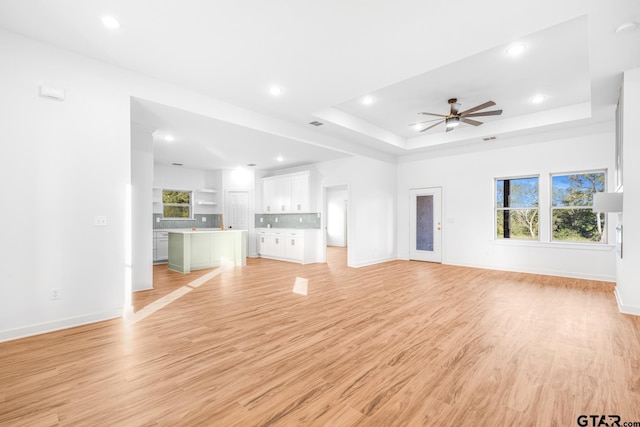 unfurnished living room with baseboards, a raised ceiling, a healthy amount of sunlight, and light wood-style flooring