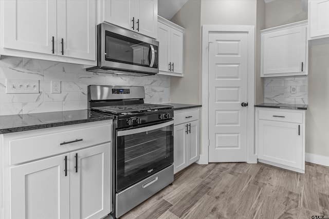 kitchen featuring stainless steel appliances, dark stone counters, white cabinetry, backsplash, and light hardwood / wood-style floors