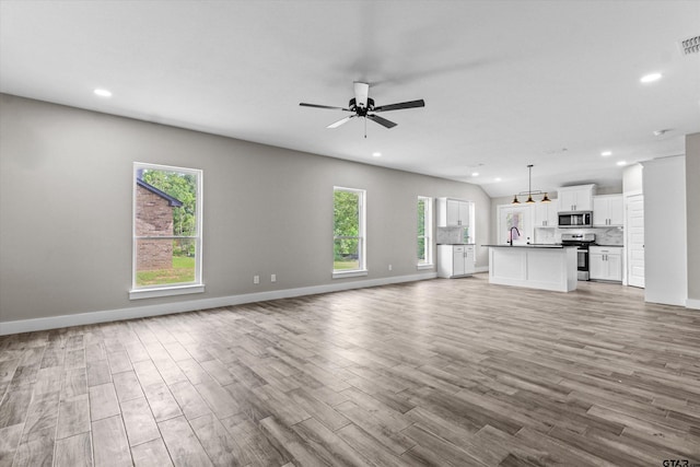 unfurnished living room featuring ceiling fan with notable chandelier and light hardwood / wood-style floors