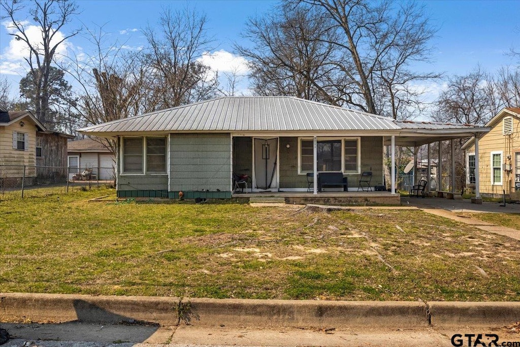 view of front of property featuring metal roof, an attached carport, covered porch, fence, and a front yard