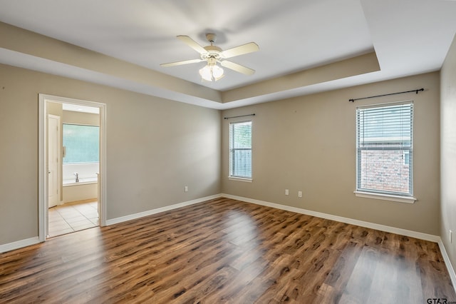 empty room featuring hardwood / wood-style floors, ceiling fan, plenty of natural light, and a tray ceiling