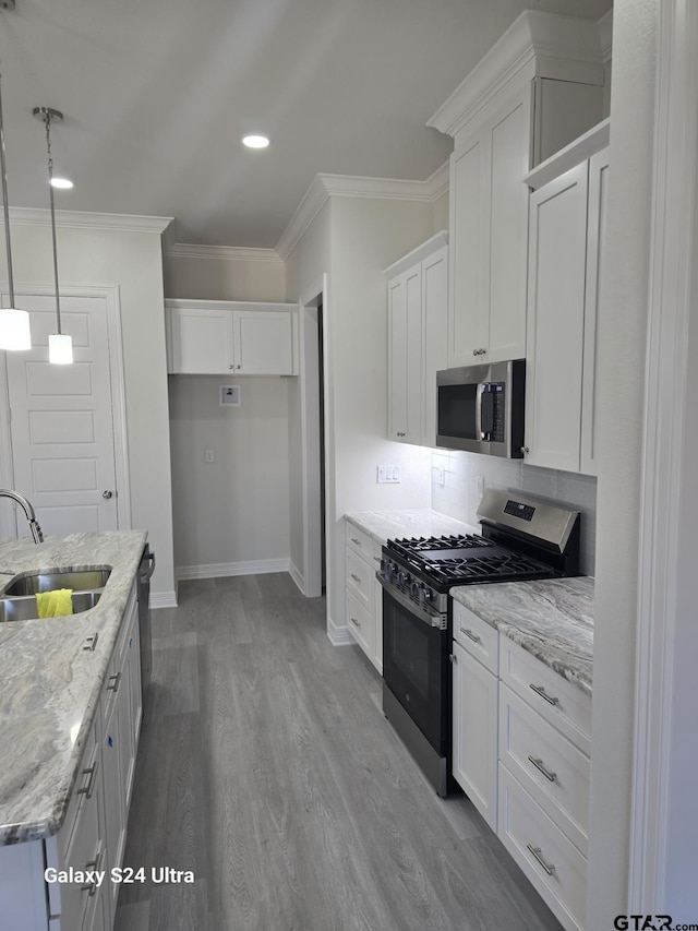 kitchen featuring sink, appliances with stainless steel finishes, white cabinetry, light stone counters, and decorative light fixtures