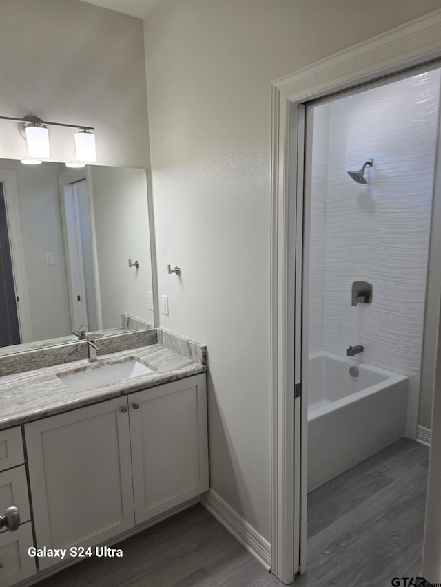 bathroom with wood-type flooring, vanity, and tiled shower / bath