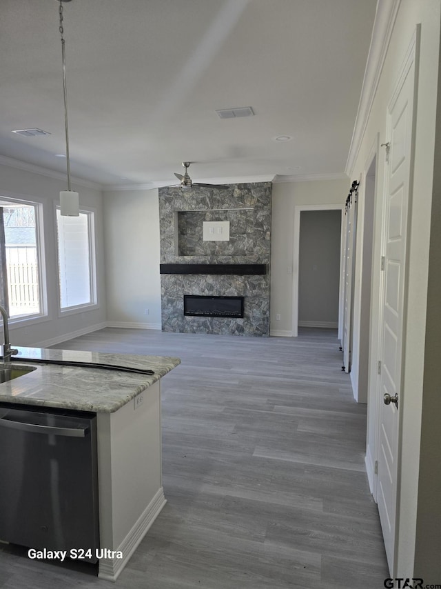 kitchen featuring a stone fireplace, dishwashing machine, hanging light fixtures, crown molding, and a barn door