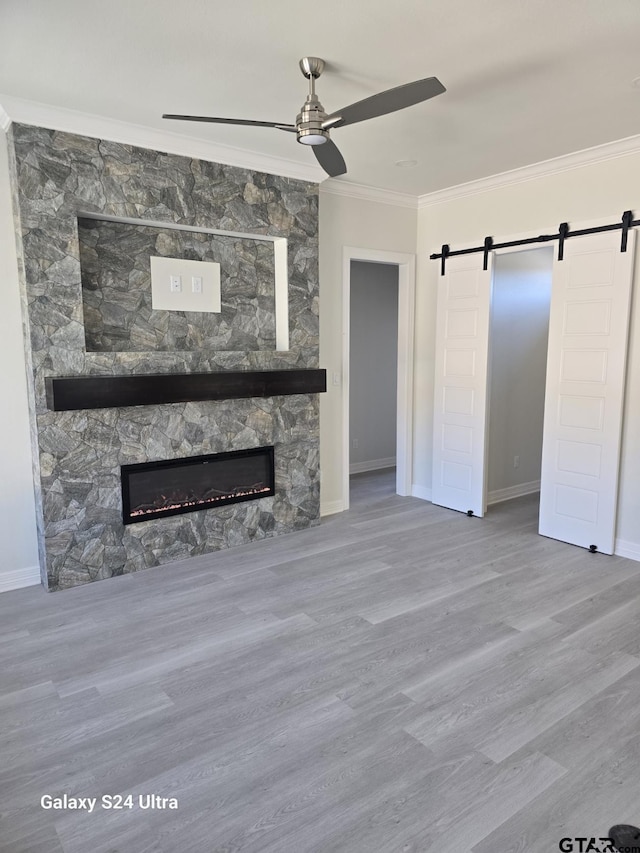 unfurnished living room with a fireplace, ornamental molding, hardwood / wood-style flooring, ceiling fan, and a barn door