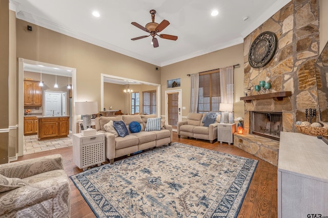 living room featuring a stone fireplace, ceiling fan with notable chandelier, ornamental molding, and light wood-type flooring