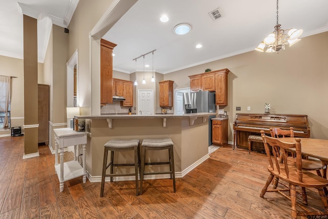 kitchen with stainless steel fridge with ice dispenser, a kitchen bar, kitchen peninsula, crown molding, and light hardwood / wood-style flooring