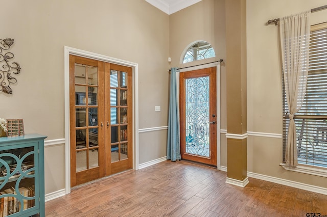 entryway with french doors, ornamental molding, a healthy amount of sunlight, and light wood-type flooring