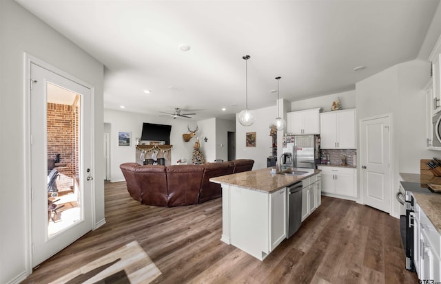 kitchen with light stone countertops, white cabinetry, dark wood-type flooring, decorative light fixtures, and a center island with sink