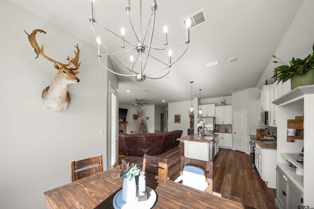 dining space with sink, dark wood-type flooring, and ceiling fan with notable chandelier