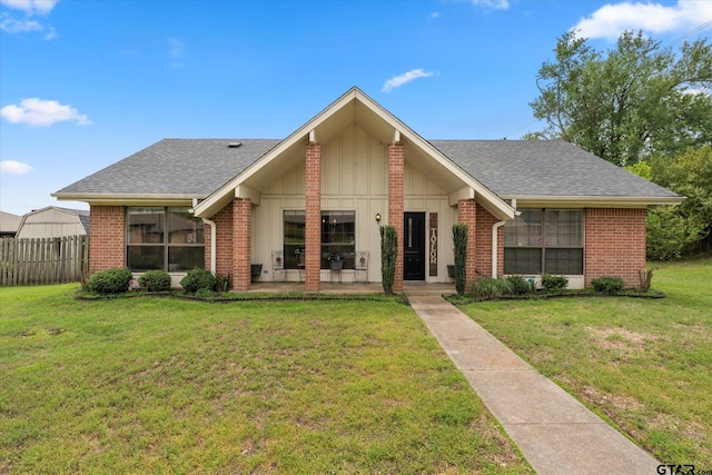 view of front of property with roof with shingles, fence, a front lawn, and brick siding