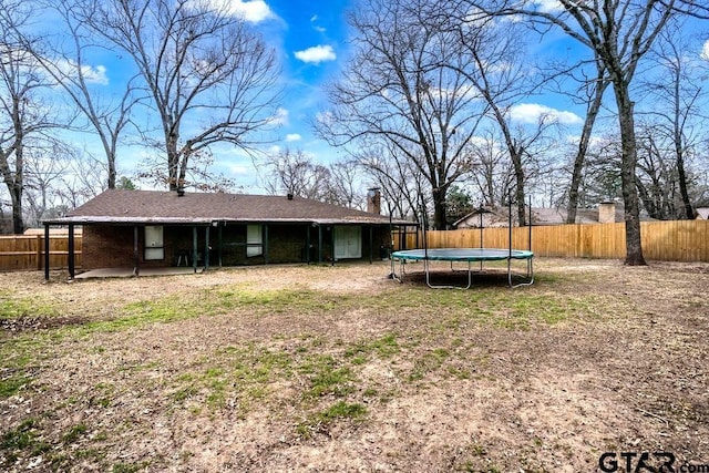 rear view of property with a fenced backyard, a trampoline, and a patio