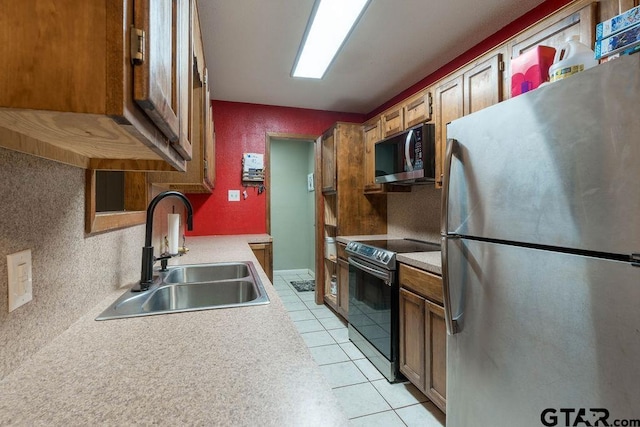 kitchen with brown cabinets, a sink, light countertops, stainless steel appliances, and light tile patterned floors
