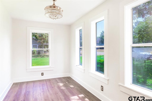 unfurnished dining area with plenty of natural light, wood-type flooring, and a notable chandelier